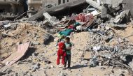 A Palestinian child walks with a stuffed bear recovered from the rubble of a destroyed building following Israeli bombardment in Khan Yunis on June 21, 2024, in the southern Gaza Strip. Photo by Eyad BABA / AFP.