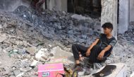 A Palestinian youth sits in the shade, on the remains of a chair placed on the rubble of buildings destroyed in previous Israeli bombardment, in the Sheikh Radwan neighbourhood, north of Gaza City on July 3, 2024. (Photo by Omar AL-QATTAA / AFP)
