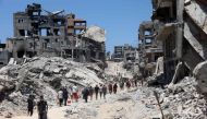 Palestinians make their way over the dirty of rubble, past destroyed buildings after the Israeli military withdrew following a two-week offensive from the Shujaiya neighbourhood, east of Gaza City on July 11, 2024. (Photo by Omar Al-Qattaa / AFP)