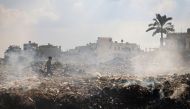  A Palestinian youth walks past piles of smouldering waste, as garbage collection and any other municipality services come to a halt due to the Israeli bombardment of the GAZA Strip, at the al-Maghazi Palestinian refugee camp, in the central GAZA Strip on July 15, 2024.(Photo by Eyad BABA / AFP)
