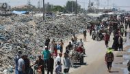 Palestinians walk past piles of garbage in Khan Yunis in the southern Gaza Strip on July 18, 2024. (Photo by Bashar Taleb / AFP)