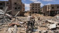 A man pushes his bicycle over rubble as displaced Palestinians return to Bani Suhayla and neighbouring towns east of Khan Yunis in the southern Gaza Strip on July 30, 2024. (Photo by Bashar Taleb / AFP)