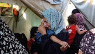 A woman carrying a child weeps following a reported overnight Israeli strike that hit tents used as temporary shelters by displaced Palestinians in the courtyard of the Al-Aqsa Martyrs hospital in Deir el-Balah in the central Gaza Strip, on August 4, 2024. (Photo by Eyad Baba / AFP)

