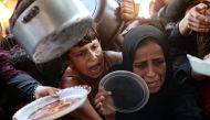 Palestinian women and children hold out their plates toward a man, to receive their share of vegetable patties prepared by volunteers in Beit Lahia in the northern Gaza Strip on August 14, 2024. Photo by Omar AL-QATTAA / AFP.