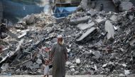 An elderly man holds a child by the hand as he walks past a building levelled by Israeli bombardment in the Bureij refugee camp in central Gaza Strip on August 25, 2024, amid the ongoing conflict between Israel and the Palestinian Hamas militant group. (Photo by Eyad BABA / AFP) 