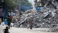 An elderly man holds a child by the hand as he walks past a building levelled by Israeli bombardment in the Bureij refugee camp in central Gaza Strip on August 25, 2024. (Photo by Eyad Baba / AFP)