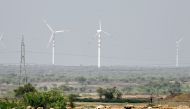 In this photograph taken on August 7, 2024, goats graze near windmills on the outskirts of Jaisalmer, in India's desert state of Rajasthan. (Photo by Idrees MOHAMMED / AFP)
