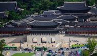 People walk past Gyeongbokgung Palace as people drive their vehicles along a main road past a statue of King Sejong (bottom L) at Gwanghwamun Square in Seoul on August 30, 2024. (Photo by ANTHONY WALLACE / AFP)
