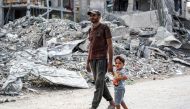 A man and child walk past the rubble of a collapsed building in Khan Yunis in the southern Gaza Strip on September 16, 2024 amid the ongoing war in the Palestinian territory between Israel and Hamas. (Photo by Bashar Taleb / AFP)