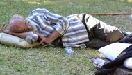 A man sleeps on the grass as displaced families who fled Israeli strikes in southern Lebanon gather at a park where they are taking refuge in Tripoli, on September 27, 2024. (Photo by Fathi Al-Masri / AFP)
