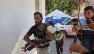 A Palestinian man rushes a child injured in Israeli military operations in northern Gaza, into Al-Ahli Arab hospital, also known as the Baptist hospital in Gaza City on October 21, 2024. (Photo by Omar Al-Qattaa / AFP)