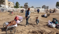 A displaced Palestinian man who fled Israeli army operations in the northern Gaza Strip, transports his belongings using a makeshift cart, in front of a newly set up tents at the Yarmouk Sports Stadium, once a football arena, in Gaza City on October 25, 2024. (Photo by Omar Al-Qattaa / AFP)
