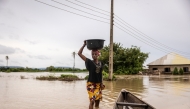 A woman balances a bucket on her head as she wades through a flooded area in Adaha, on October 22, 2024. Photo by OLYMPIA DE MAISMONT / AFP.