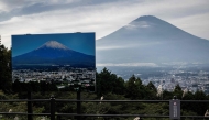 A sign with a photo of Mount Fuji covered in snow is seen at a view point as Mount Fuji, the highest mountain in Japan at 3,776 metres, looms in the background in Gotemba, Shizuoka prefecture on October 31, 2024. Photo by Yuichi YAMAZAKI / AFP