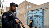 This photograph taken on October 29, 2024 shows an elite police personnel (L) standing guard as a health worker marks houses with numbers during a door-to-door poliovirus vaccination campaign for children on the outskirts of Peshawar. (Photo by Abdul MAJEED / AFP)
