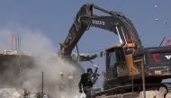 A member of the Israeli security forces walks past a bulldozer demolishing a house belonging to Palestinians, located in the area C, which lies under Israel's military control since 1967, in Yatta village in the southern area of the occupied West Bank, on November 6, 2024. (Photo by HAZEM BADER / AFP)
