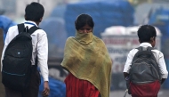 A woman covers her face as she walks past school boys on a cold smoggy morning in the old quarters of New Delhi on November 15, 2024. (Photo by Arun SANKAR / AFP)