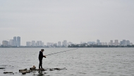 A man stands on rocks as he fishes in West Lake in Hanoi on November 27, 2024. Photo by Nhac NGUYEN / AFP