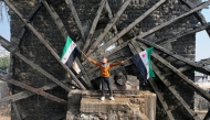 Photo used for representation purposes. A boy waves the opposition Syrian flag as he stands in one of the water wheels, or norias, in Hama, after anti government fighters captured of the central city, on December 6, 2024. Photo by Omar HAJ KADOUR / AFP.