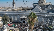 This aerial view shows pigeons flying as people crowd outside the 8th-century Umayyad mosque and the Hamidiyah covered market in the old city of Damascus on December 13, 2024 during first weekly Muslim Friday prayers since the ouster of president Bashar al-Assad. Photo by Bakr ALKASEM / AFP.