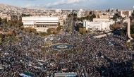 This aerial view shows people celebrating the ouster of Syria's president Bashar Al Assad near the landmark Damascus Sword sculpture at the Umayyad Square in central Damascus on December 13, 2024. (Photo by Sameer Al-Doumy / AFP)