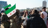 Rebel fighters stand near protesters during a student rally near the campus of the Damascus University in the Syrian capital on December 15, 2024. Photo by Omar HAJ KADOUR / AFP.