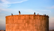 Children sit at sunset atop a concrete water storage tank overlooking the Hamad Residential City complex in the north of Khan Yunis in the southern Gaza Strip on December 22, 2024. (Photo by Bashar Taleb / AFP)