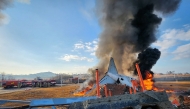 Fire and smoke rise from the tail section of a Jeju Air Boeing 737-800 series aircraft after the plane crashed and burst into flames at Muan International Airport in South Jeolla Province, some 288 kilometres southwest of Seoul on December 29, 2024. (Photo by YONHAP / AFP) 