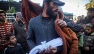 A Muslim cleric wraps a blanket around the father of newborn Jumaa al-Batran, who reportedly died due to hypothermia, as the latter holds the baby's shrouded body ahead of the funeral at the Aqsa Martyrs hospital in Deir el-Balah in the central Gaza Strip on December 29, 2024. (Photo by Eyad BABA / AFP)