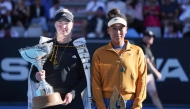 Clara Tauson of Denmark (L) celebrates with the trophy after her win over Naomi Osaka of Japan (R), following Osaka's retirement from their women's singles final match due to an abdominal injury, at the WTA Auckland Classic tennis tournament in Auckland on January 5, 2025. (Photo by Michael Bradley / AFP)