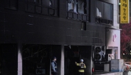 Firefighters and a police officer stand in front of a commercial building that was damaged by a fire that broke out at the Bundang district in Seongnam on January 3, 2025. (Photo by Philip FONG / AFP)
