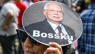 A woman holds a hand fan bearing a photo of former Malaysia's prime minister Najib Razak and reading 