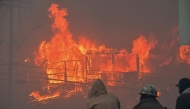 Three men watch as a house is engulfed in flames from the wind-driven Palisades Fire in Pacific Palisades, California, January 7, 2025. (Photo by Robyn Beck / AFP)