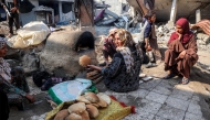 A woman bakes bread in a clay oven by collapsed buildings in Deir el-Balah in the central Gaza Strip on January 12, 2025 amid the ongoing war in the Palestinian territory. Photo by Eyad BABA / AFP.
