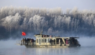 This photo taken on January 12, 2025 shows a boat sailing on Songhua River as visitors gather to see the frost-covered trees on the riverbank in Jilin, northeast China's Jilin province. (Photo by AFP) 