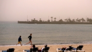 Children run along the beach as people look over the sea into the haze created by a sand storm known locally as 