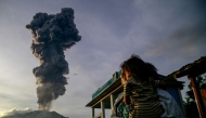 A woman and child look on at volcanic ash rising into the air during the eruption of Mount Ibu, as seen from Duono Village in West Halmahera, North Maluku province, on January 15, 2025. (Photo by AZZAM / AFP)