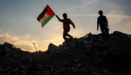 A boy runs with a Palestinian flag atop a mound of rubble at a camp for people displaced by conflict in Bureij in the central Gaza Strip on January 17, 2025. (Photo by Eyad Baba / AFP)
