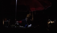 A woman sits by a lamp at her stall in Goma on January 24, 2025, as the rest of the market is plunged into obscurity following a powerline damage . (Photo by Jospin Mwisha / AFP)
 