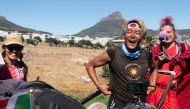 Gump Suzuki (C), the Japanese runner and social media sensation who started in July 2024 an overland journey of 6400km from Kenya to South Africa, reacts with members of his support team as he takes a rest on the side of a highway from pushing his rickshaw as he nears his end-goal at the Waterfront in Cape Town on January 26, 2025. (Photo by RODGER BOSCH / AFP)
