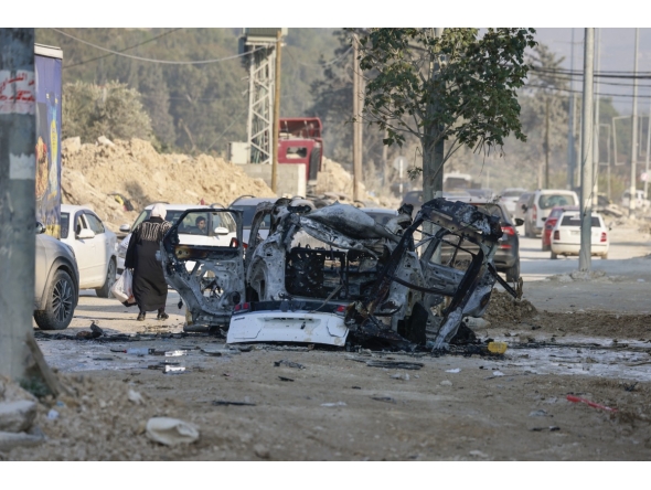 Palestinians drive their vehicles past the carcass of a car that was destroyed in an Israeli airstrike in the Nur Shams refugee camp near Tulkarem in the occupied West Bank on January 27, 2025. (Photo by Jaafar ASHTIYEH / AFP)
