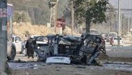 Palestinians drive their vehicles past the carcass of a car that was destroyed in an Israeli airstrike in the Nur Shams refugee camp near Tulkarem in the occupied West Bank on January 27, 2025. (Photo by Jaafar ASHTIYEH / AFP)
