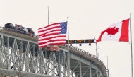 (Files) The US and Canadian flags fly on the US side of the St. Clair River near the Bluewater Bridge border crossing on January 29, 2025. (Photo by Geoff Robins / AFP)