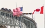 (Files) The US and Canadian flags fly on the US side of the St. Clair River near the Bluewater Bridge border crossing on January 29, 2025. (Photo by Geoff Robins / AFP)