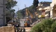 People and soldiers watch an excavator clearing the rubble from a street in the southern Lebanese border town of Aitaroun, as inhabitants return following the pullout of Israeli troops and the deployment of the Lebanese army, on February 2, 2025. (Photo by Mahmoud ZAYYAT / AFP)