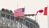 (FILES) The US and Canadian flags fly on the US side of the St. Clair River near the Bluewater Bridge border crossing between Sarnia, Ontario and Port Huron, Michigan on January 29, 2025. (Photo by Geoff Robins / AFP)
