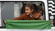 A girl holds an independence-era Syrian flag out of the window of a bus carrying displaced Syrians returning home after years of displacement in the northern Aleppo province, at the entrance of the central city of Homs on February 10, 2025. (Photo by Louai Beshara / AFP)