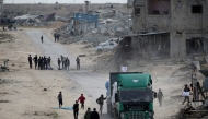 Palestinians rush to collect bottles of water that fell from a truck loaded with humanitarian aid as it drives through Rafah in the southern Gaza Strip after crossing through the Kerem Shalom crossing on February 18, 2025. (Photo by Eyad BABA / AFP)
