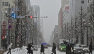 This photo taken on February 18, 2025 shows pedestrians crossing the street in the snow in central Sapporo, Hokkaido prefecture. (Photo by Richard A. Brooks / AFP)