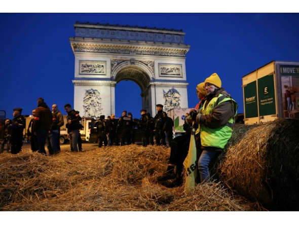 (Files) French farmers are seen sitting on a bale of hay as policemen secure the area in front of the Arc de Triomphe near the Champs-Elysees Avenue during a protest by the French farmers' union in Paris on March 1, 2024. (Photo by Thomas Samson / AFP)